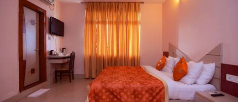 Habitación de hotel con cama, escritorio, silla, televisor y ventana con cortinas.