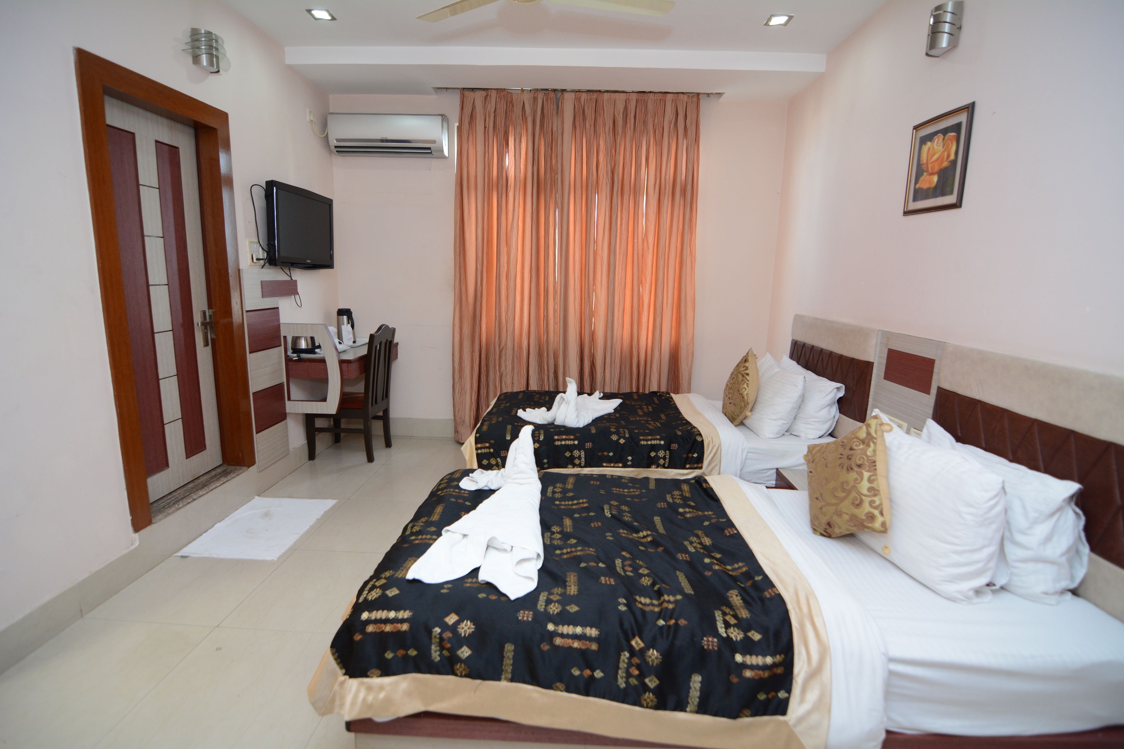 A hotel room with two beds, a desk with a chair, a television, and an air conditioning unit.