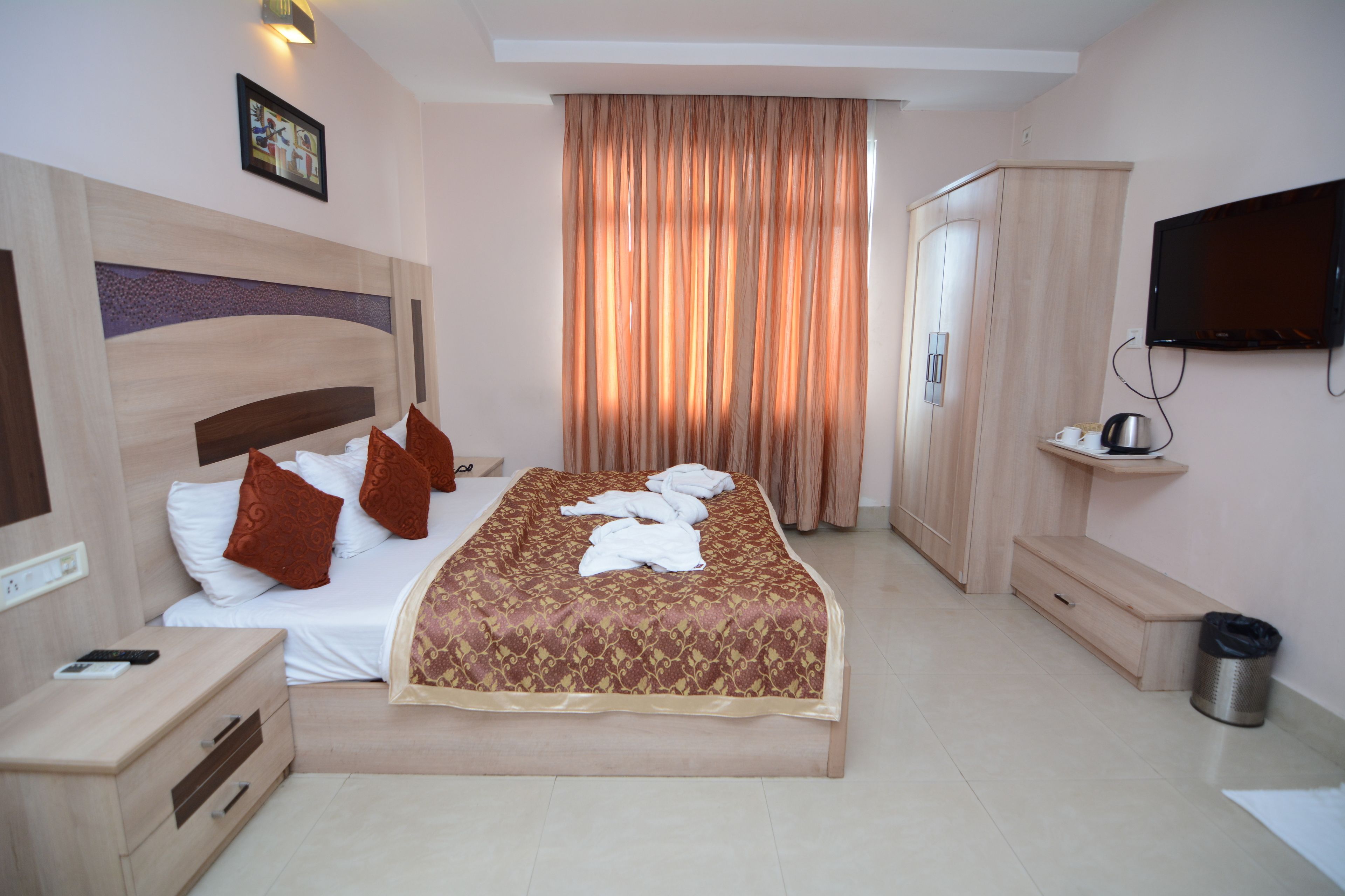 Habitación de hotel con cama, mesita de noche, televisor, armario y cortina.