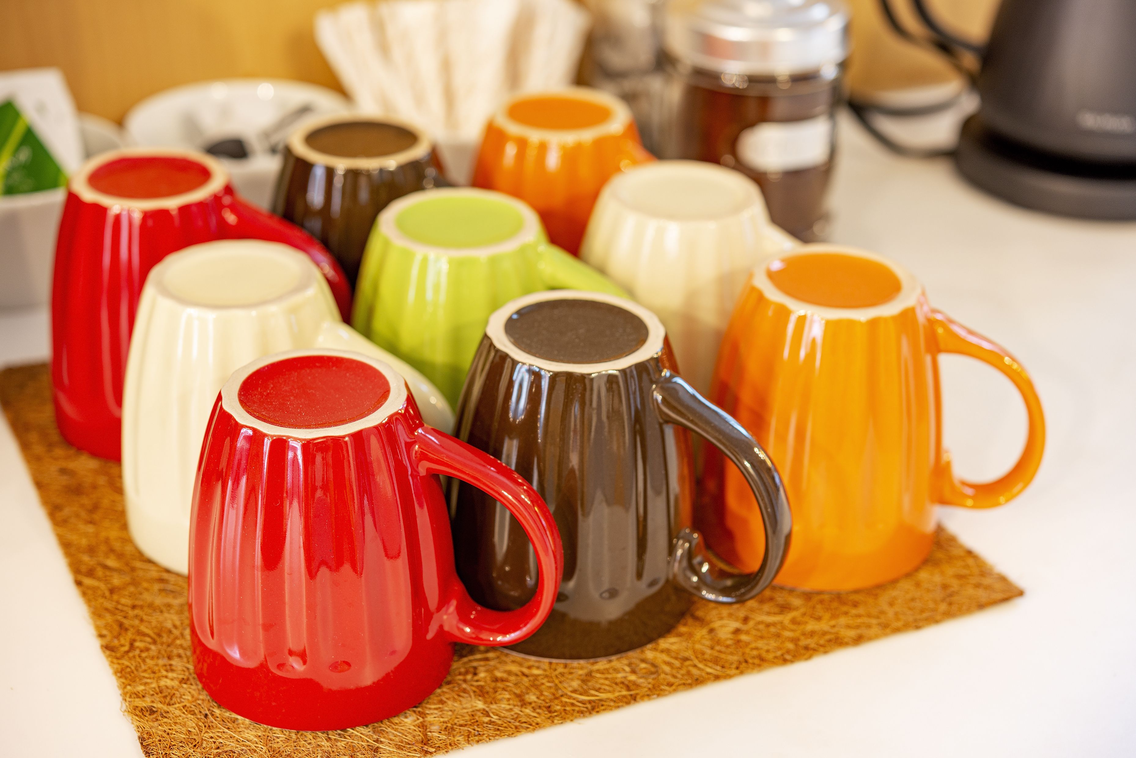 Une collection de tasses en céramique aux couleurs vives, disposées sur un set de table en fibres tressées.
