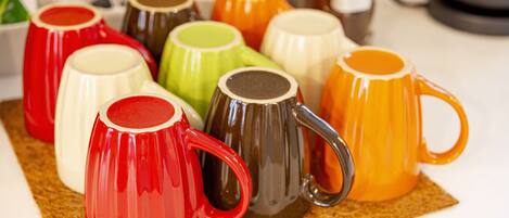 Une collection de tasses en céramique aux couleurs vives, disposées sur un set de table en fibres tressées.