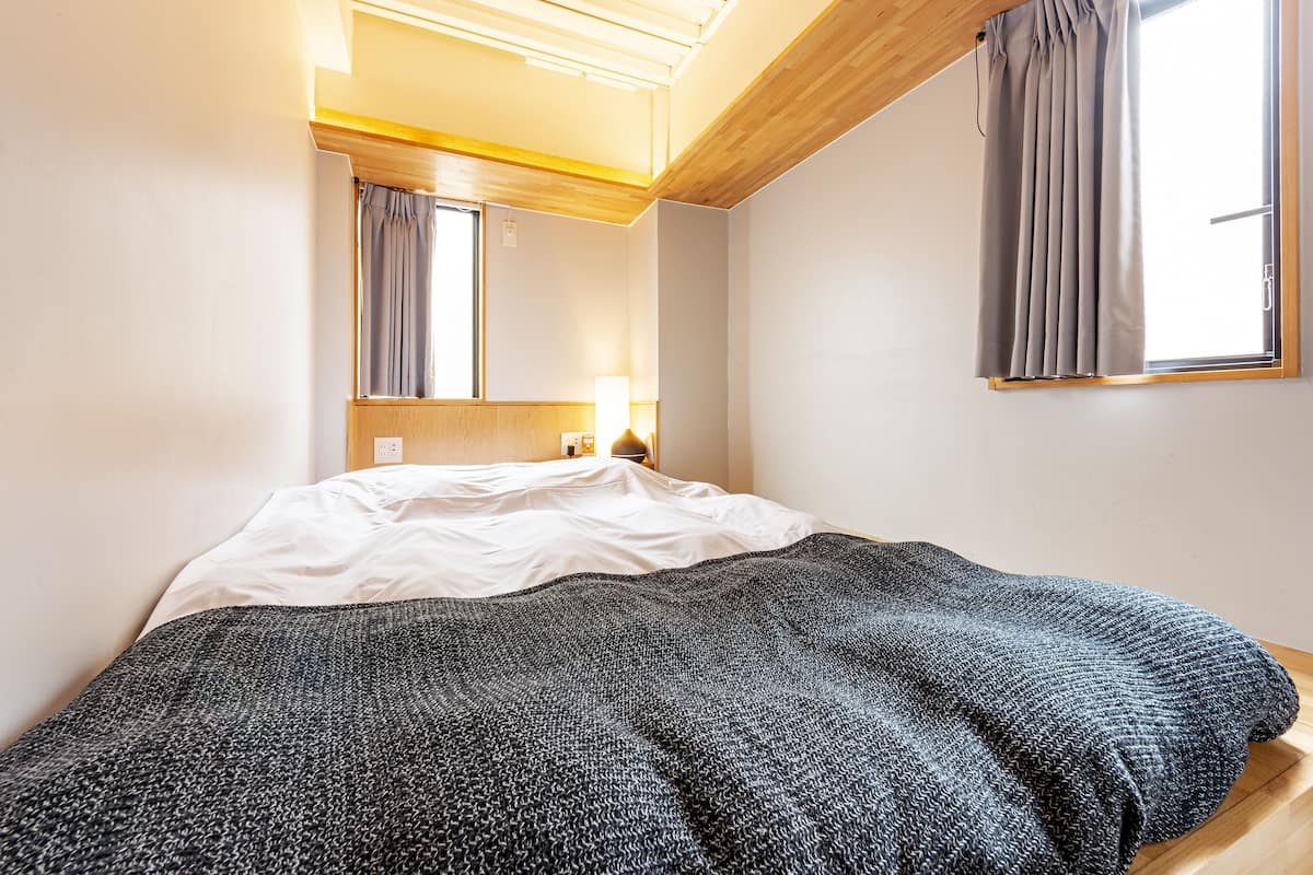 Un dormitorio con una cama, una lámpara de noche, un ventanal con cortinas y techo de madera.