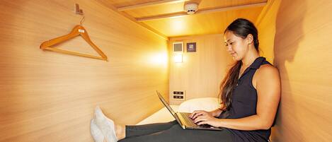 A woman sitting on a bed in a room with wooden walls, using a laptop.