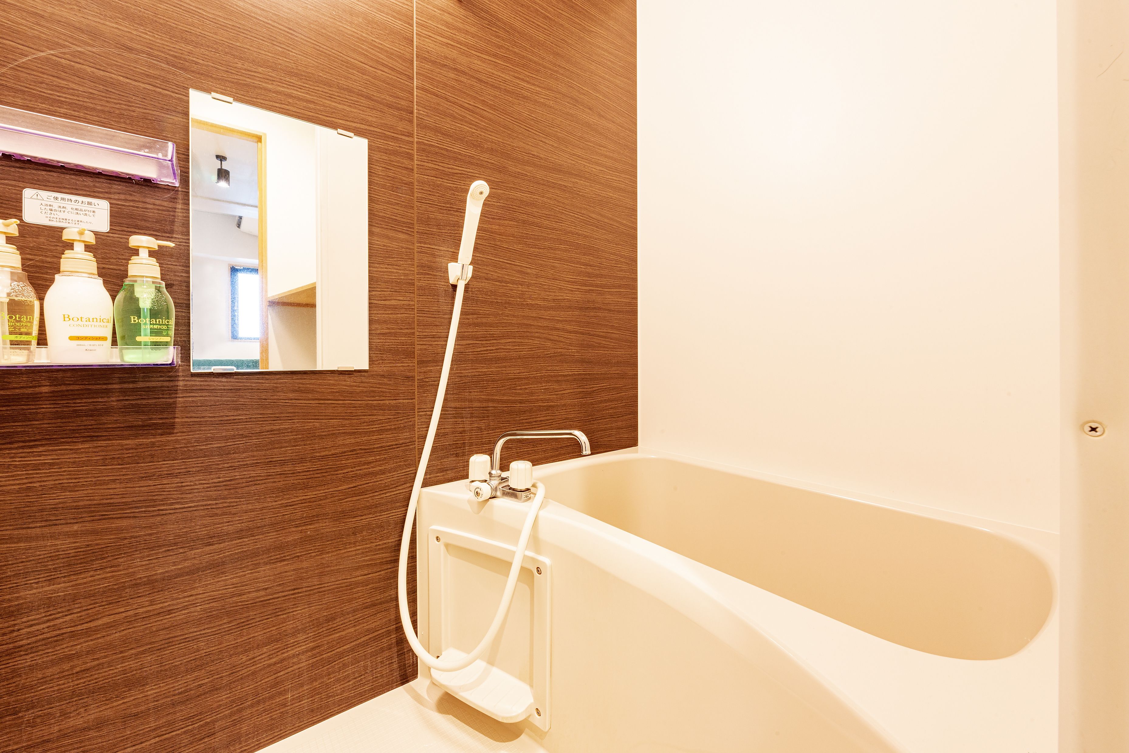 A bathroom with a bathtub, a shower, and a mirror. There are bottles of toiletries on a shelf.