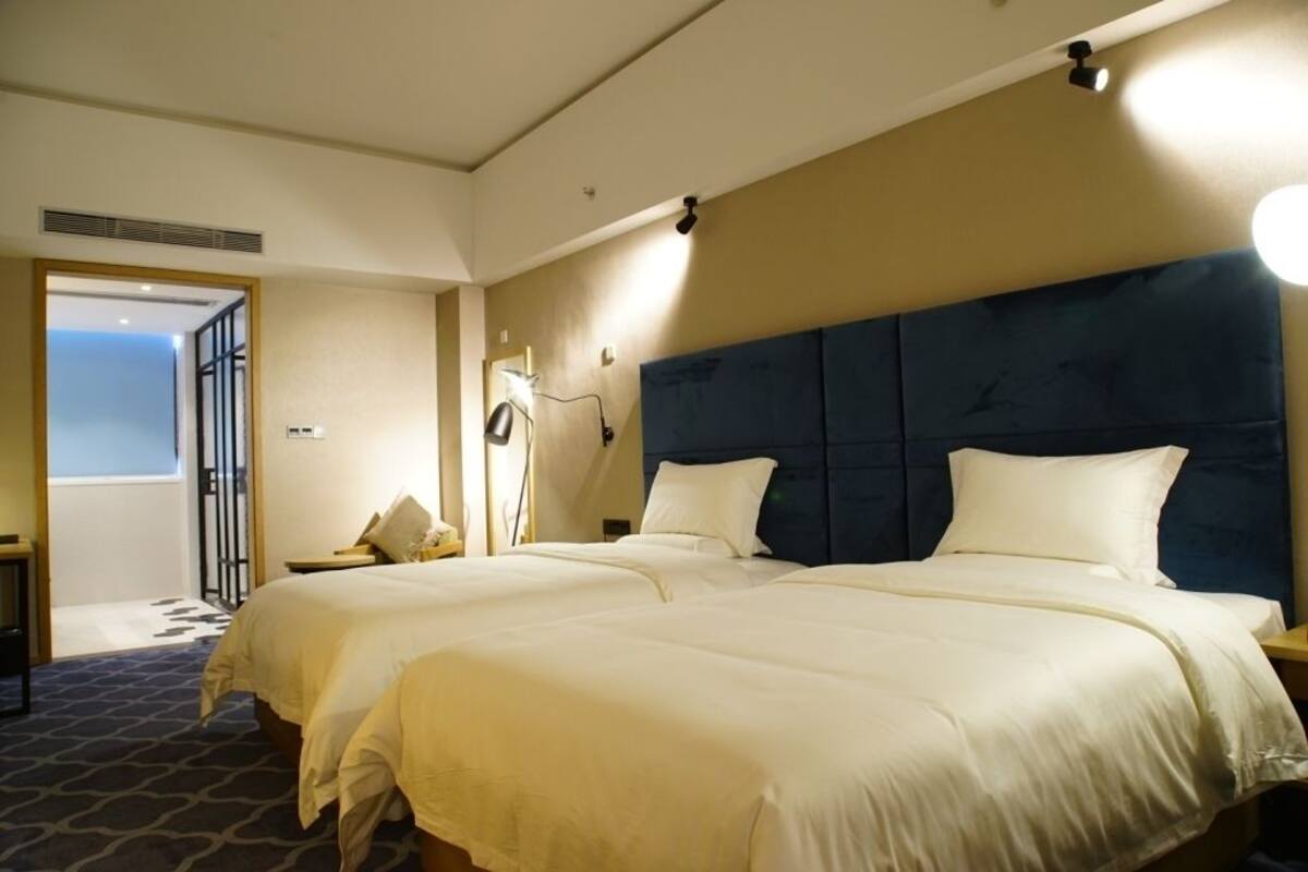 A hotel room with two beds, a large headboard, bedside lamps, and a view of the outside.