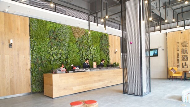 A reception area with a wooden desk, a green wall with plants, and a modern design. - One Flight Apartment Bao'an Branch (Shenzhen)