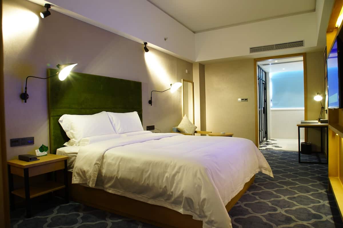 A hotel room with a large bed, bedside tables, a nightstand, a lamp, a mirror, and a television.