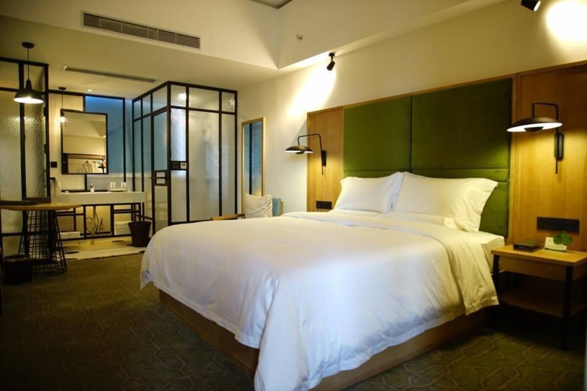 A hotel room with a large bed, a desk with a chair, a mirror, and a green headboard.