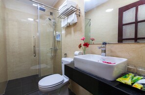 A bathroom with a glass shower enclosure, a toilet, a sink with a large mirror, and a towel rack. - Hanoi Elpis Hotel (Hanoi)