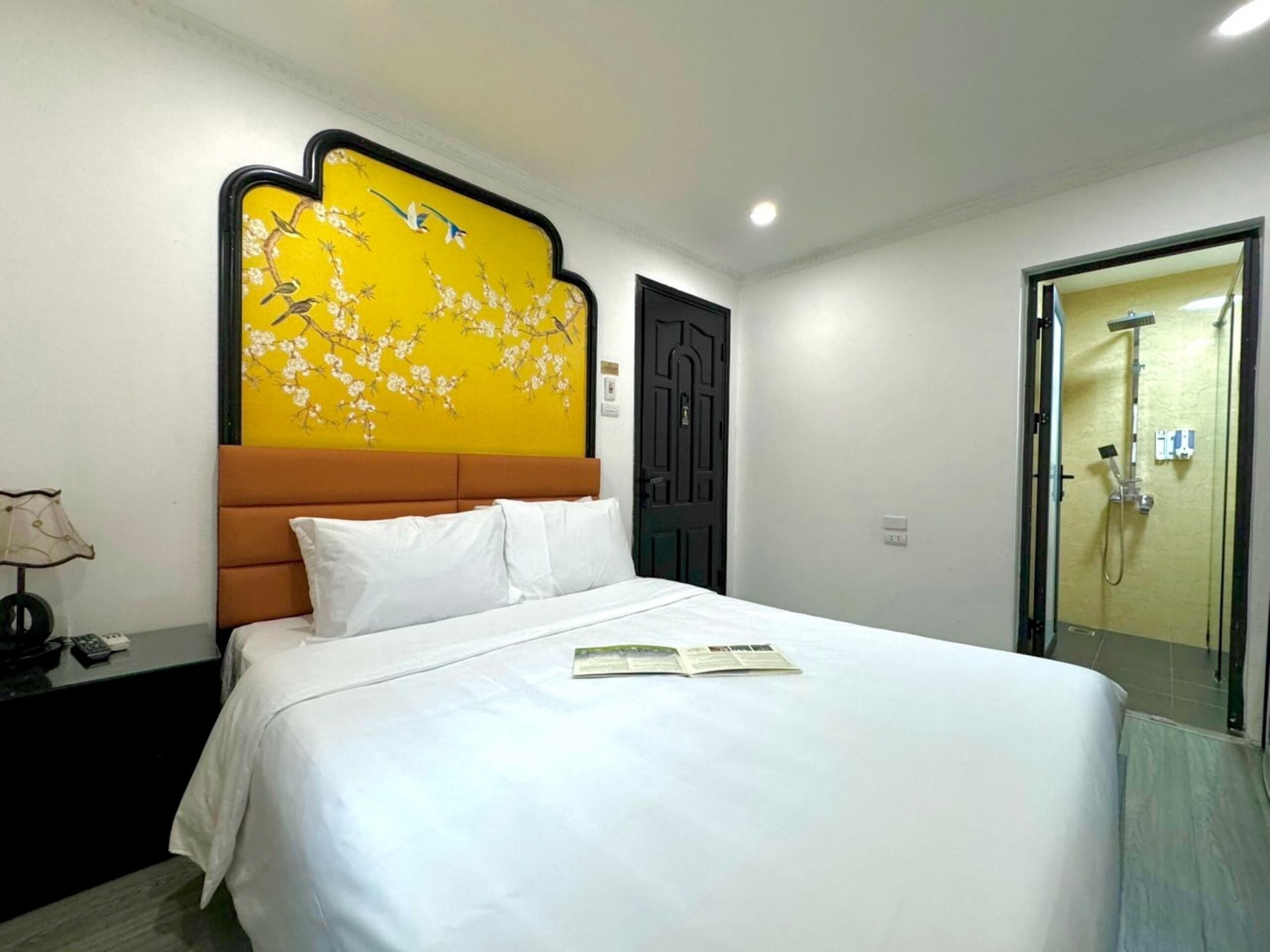 A hotel room with a bed, a nightstand, a lamp, a door, and a shower area.