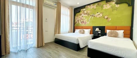 A hotel room with two beds, a large window with curtains, an air conditioning unit, and a floral mural on the wall.