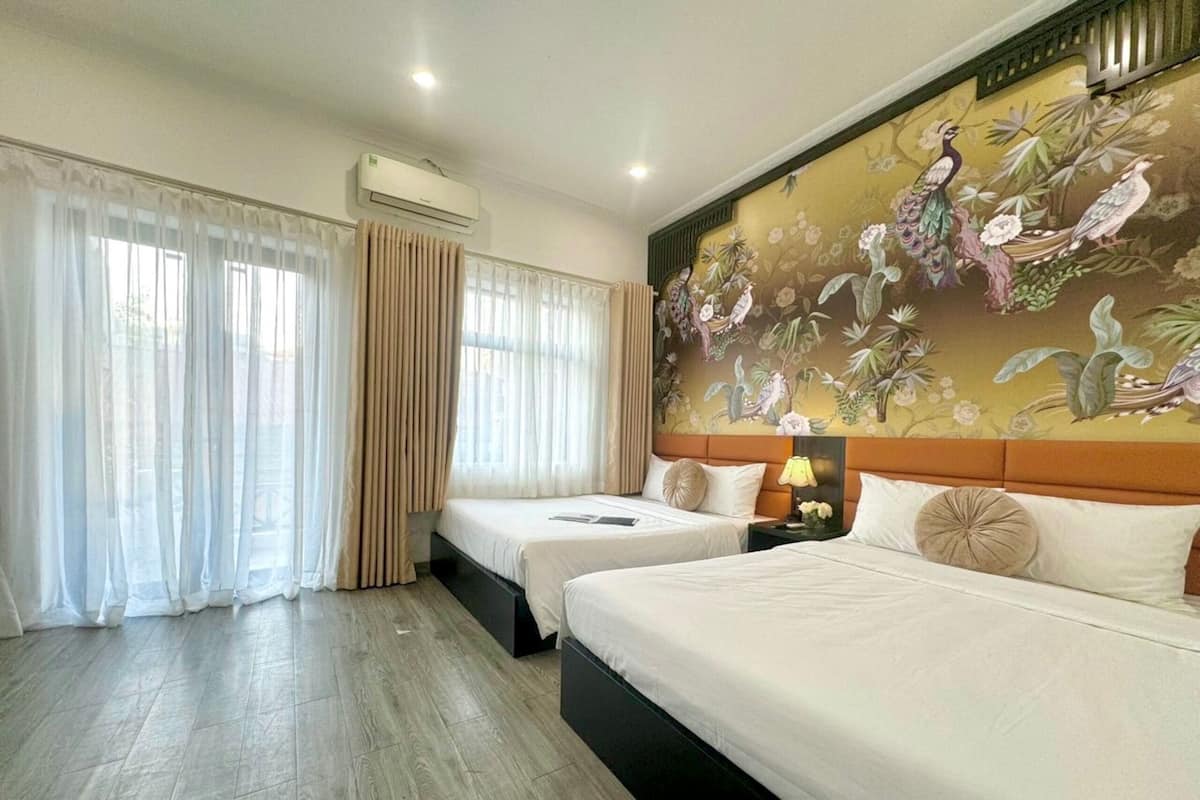 Une chambre d’hôtel avec deux lits, une grande fenêtre avec des rideaux légers, un appareil de climatisation et une fresque florale sur le mur.