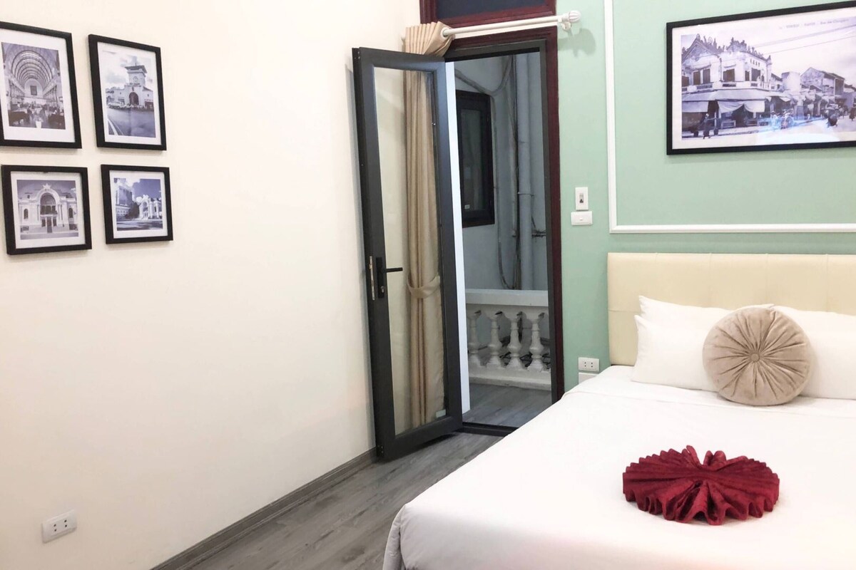 A bedroom with a bed, a door leading to a balcony, and framed pictures on the wall.