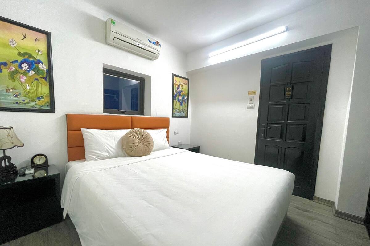 Une chambre d’hôtel avec un lit, un climatiseur, une fenêtre et des œuvres d’art accrochées aux murs.