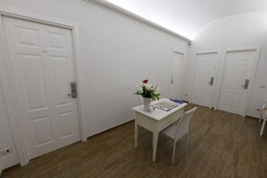 A hallway with white doors, a white table with a vase of flowers, and a chair. - Buonanotte Roma 2 (Rome)