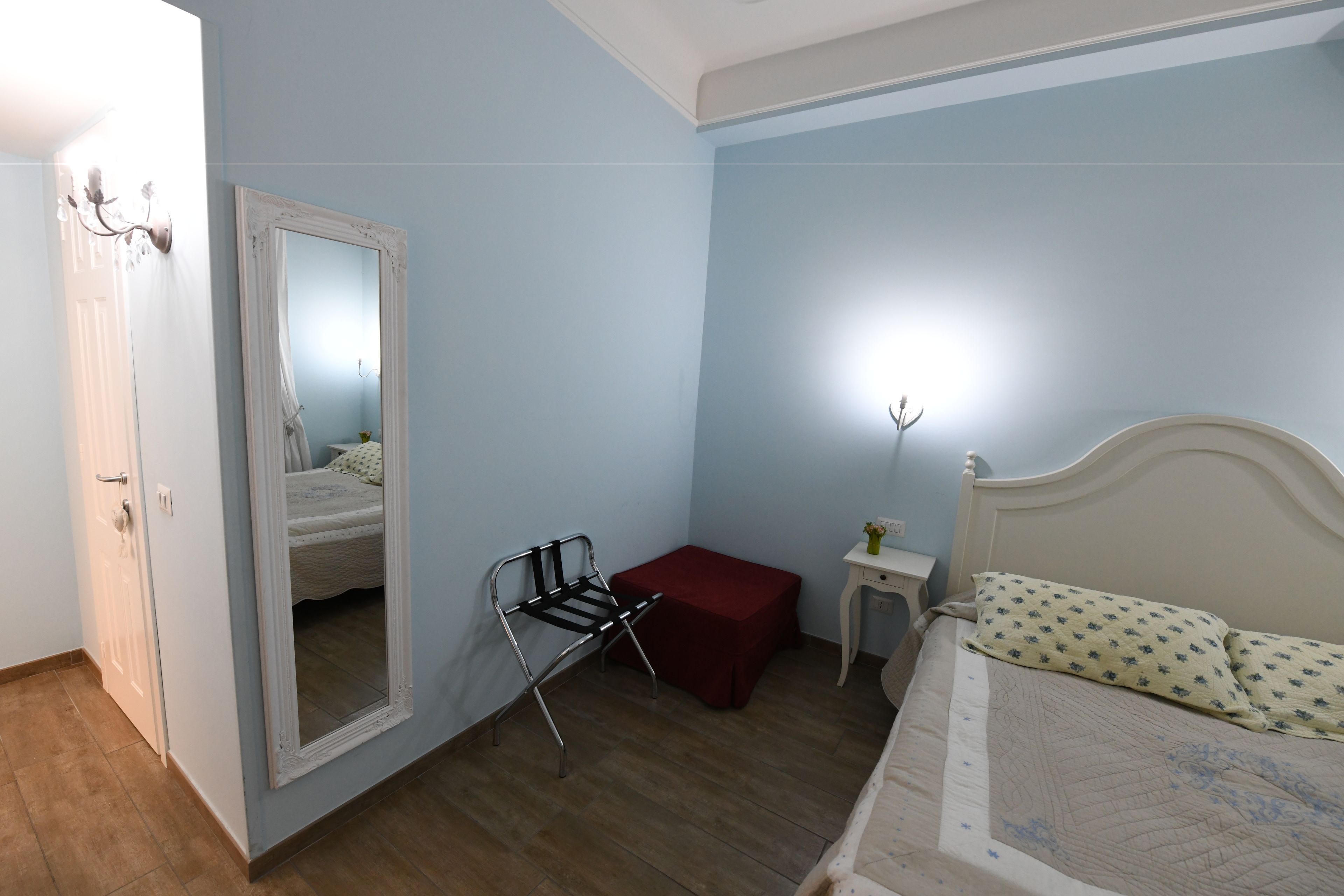 A bedroom with a bed, a chair, a small table, and a mirror.