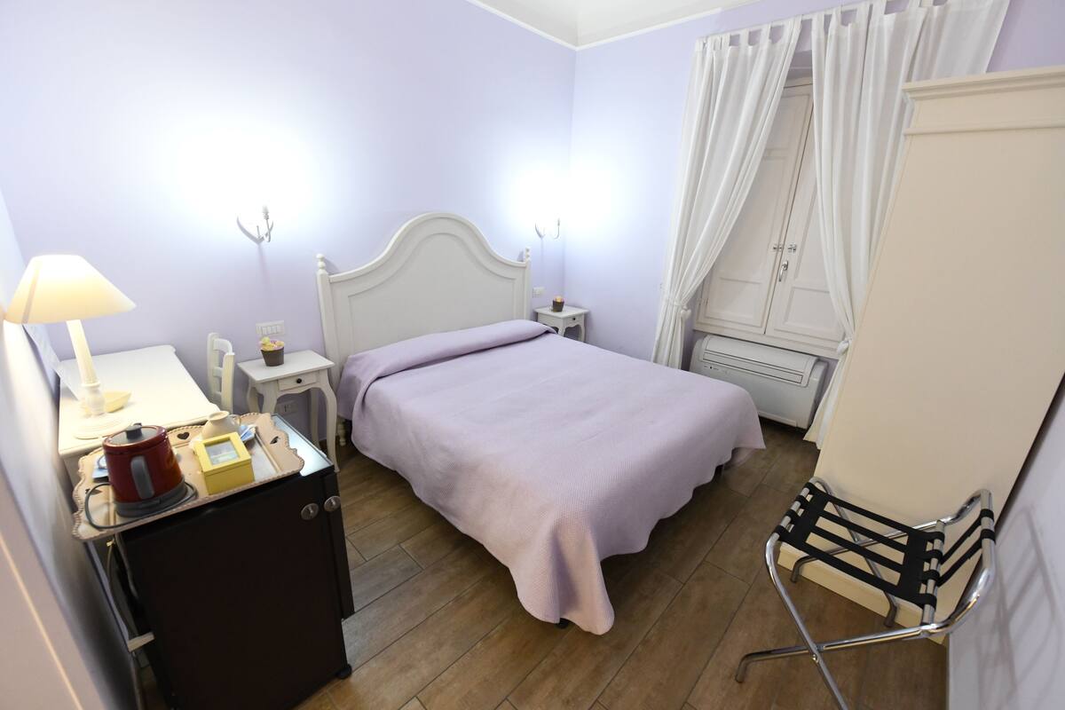 A bedroom with a bed, bedside table, lamp, and a small cabinet.