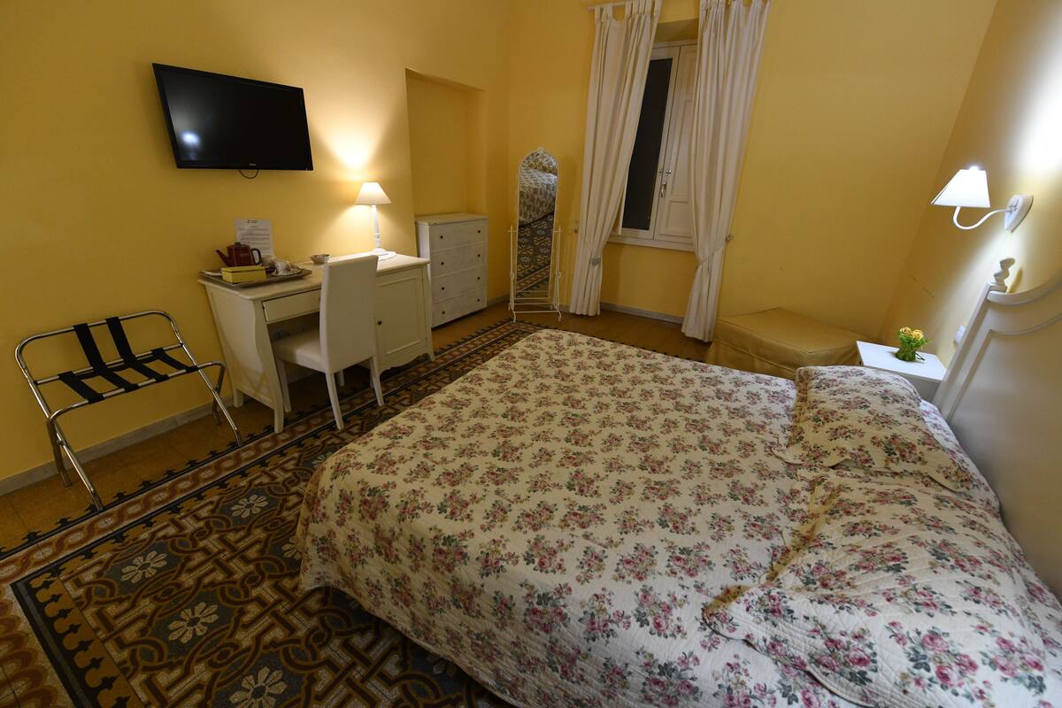 A hotel room with a bed, desk, chair, and a television on the wall.