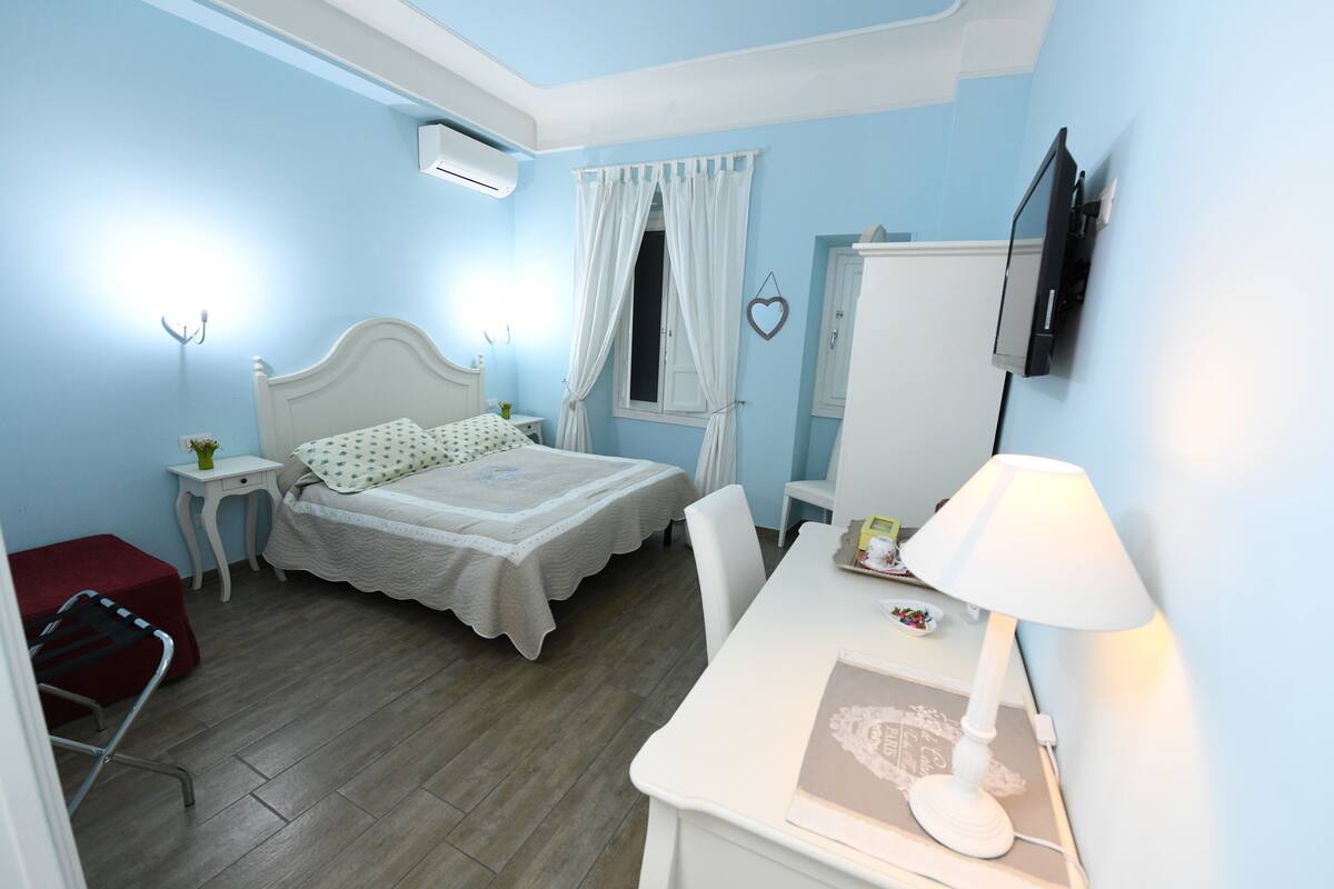 A bedroom with a bed, bedside table, lamp, and a TV mounted on the wall.