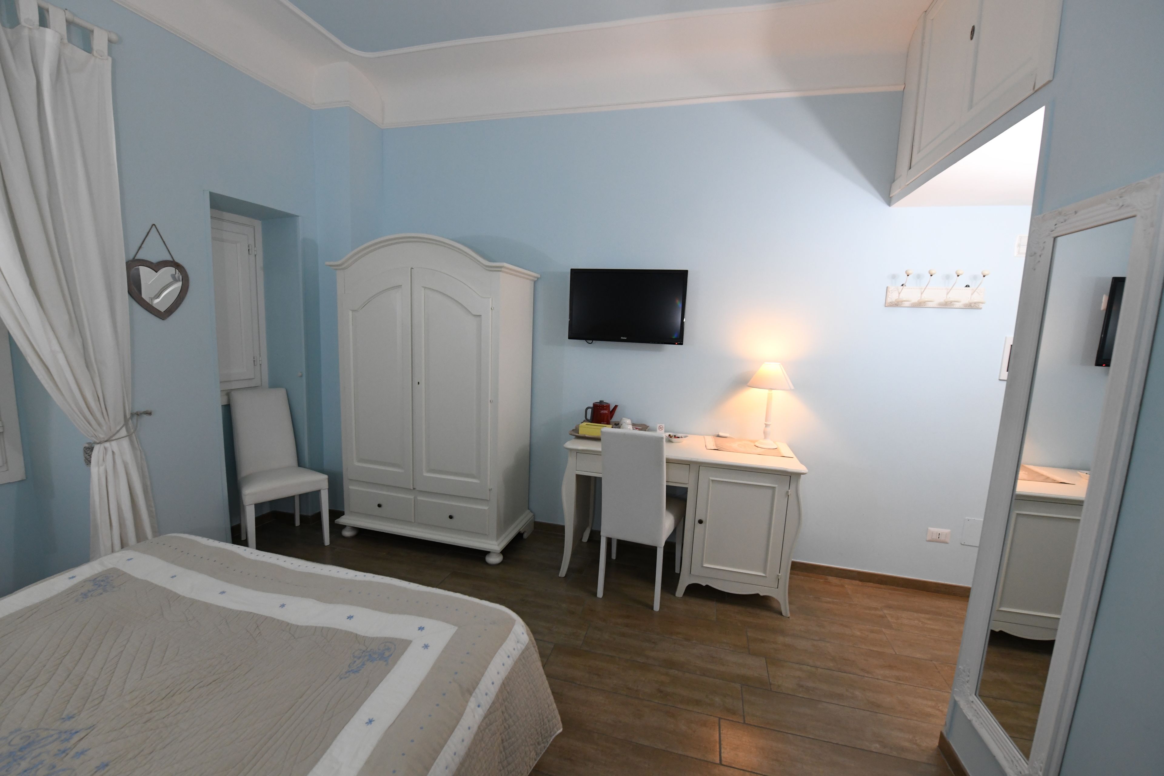 A bedroom with a bed, a desk, a chair, a wardrobe, a television, and a mirror.