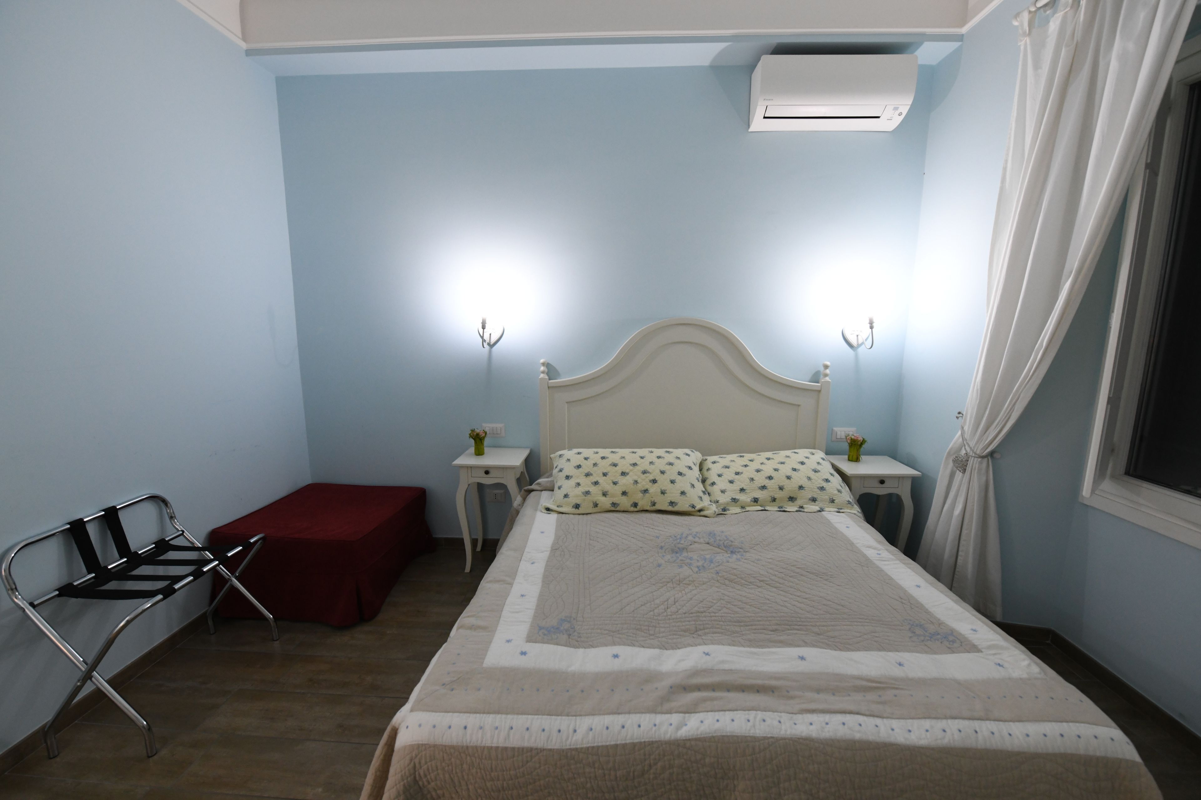 A bedroom with a bed, a bench, a nightstand, and an air conditioning unit.
