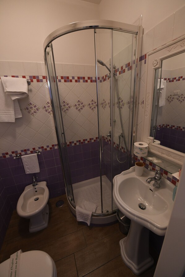 A bathroom with a glass shower enclosure, a bidet, a sink, and a toilet.