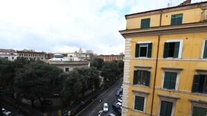 A yellow building with multiple windows and balconies, a street with parked cars, and trees in the foreground. - Buonanotte Roma 2 (Rome)