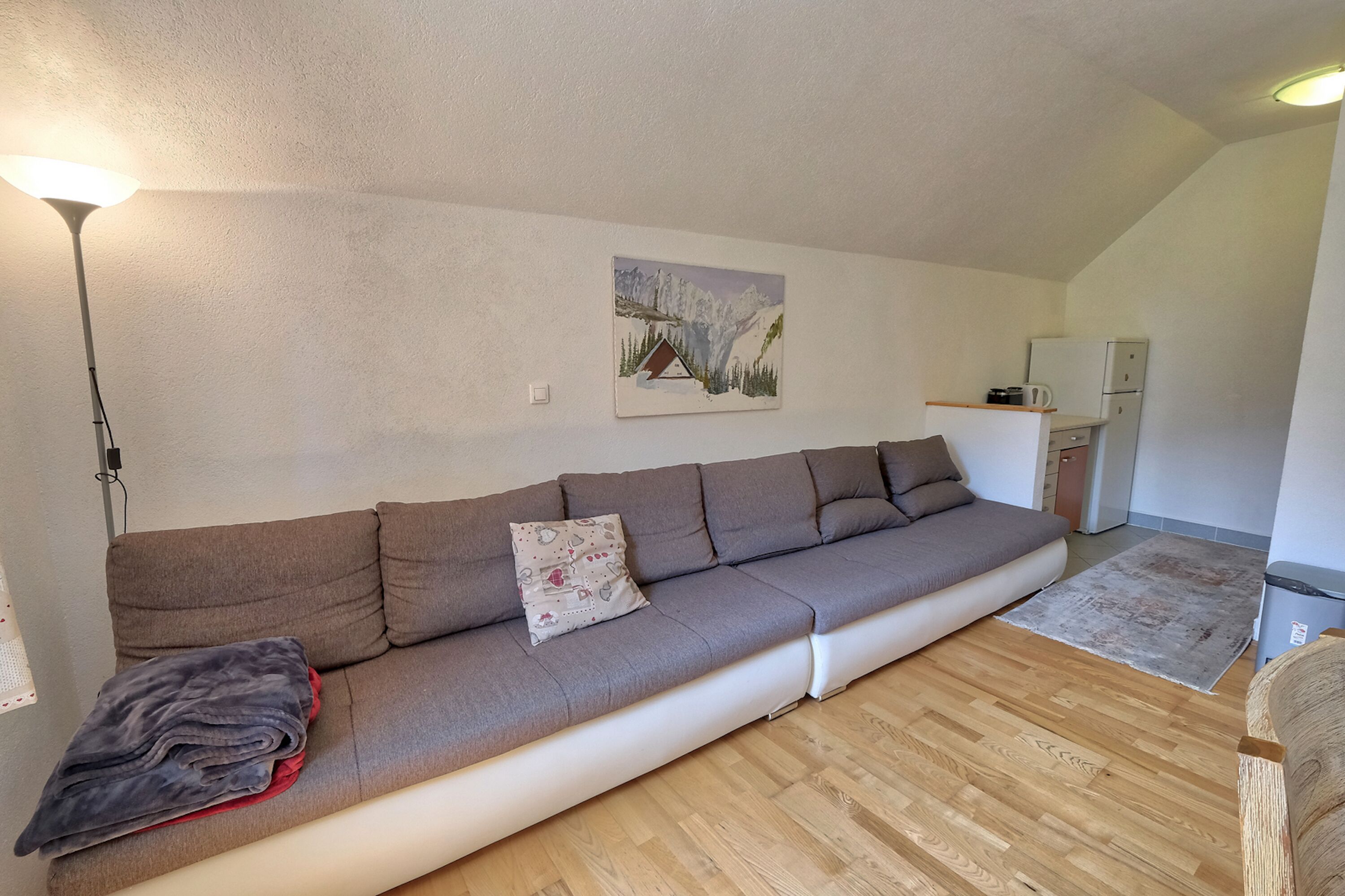 A modern living room with a sofa, a painting, a lamp, and a kitchen area.