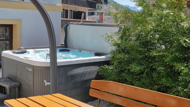 A hot tub with a wooden bench in front, a balcony, and a view of a mountain range. - Jacob´s Resort House Podkoren (Kranjska Gora)