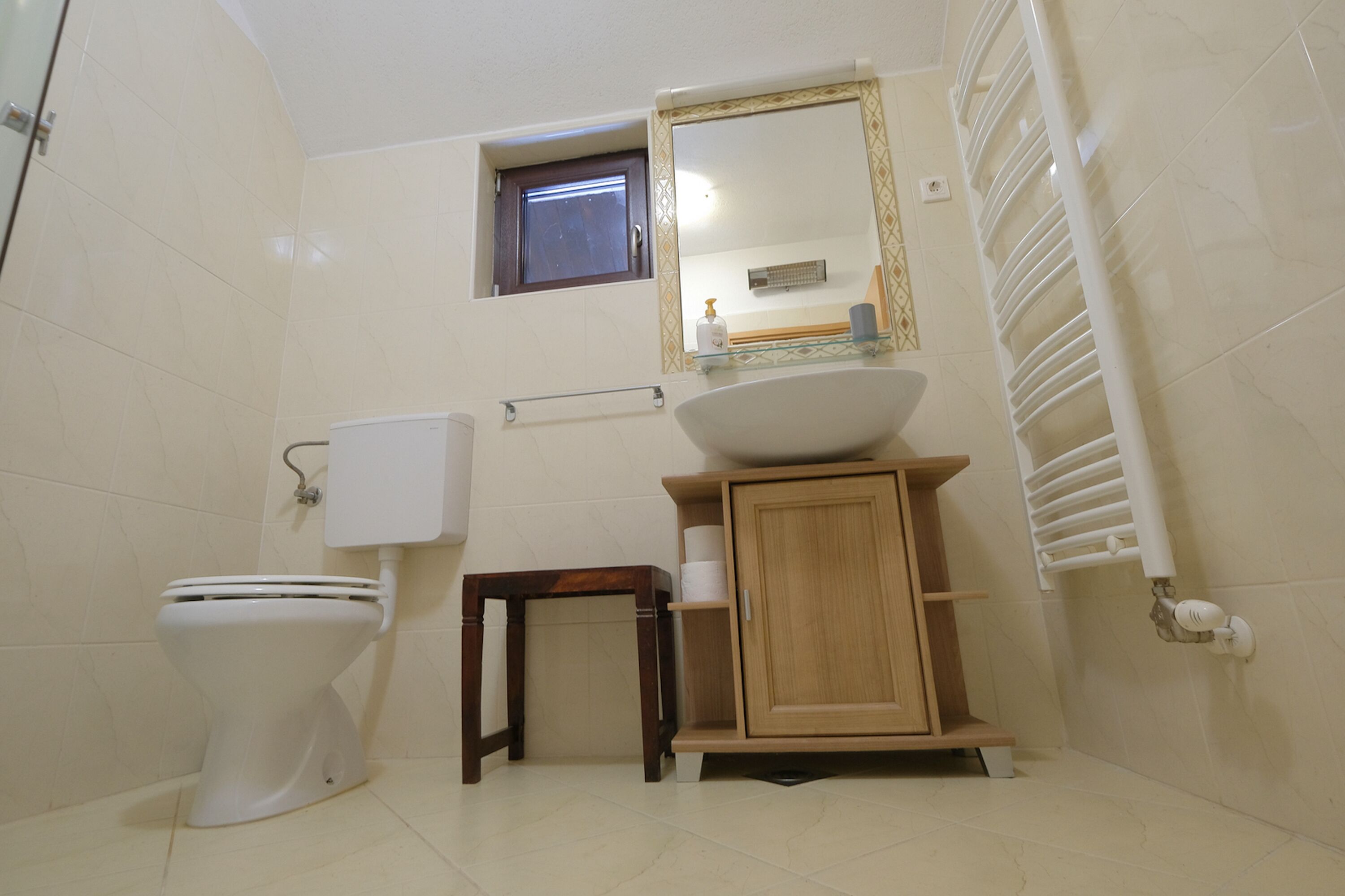 A bathroom with a toilet, a sink with a mirror above, a small window, and a towel rack.