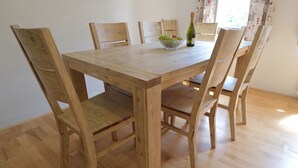 A wooden dining table with six chairs, a bowl of fruit, and a bottle of wine. - Jacob´s Resort House Podkoren (Kranjska Gora)