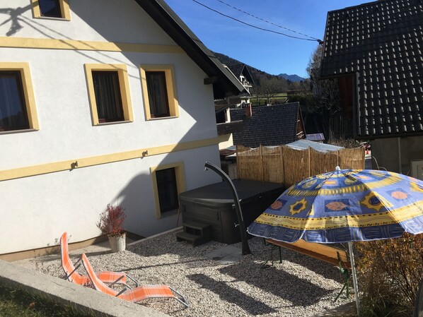 Una casa con fachada blanca y detalles amarillos, un patio con mesa y sillas, y un paraguas con diseño.