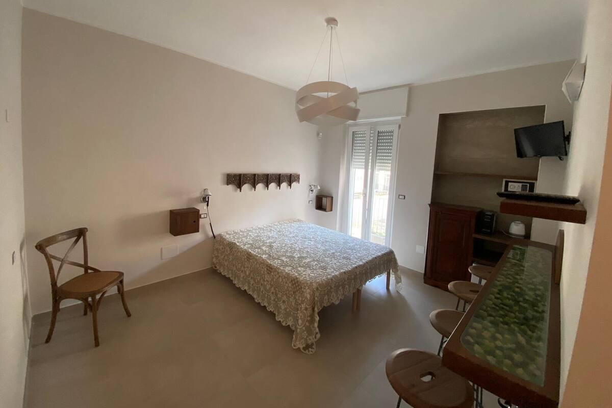 A bedroom with a bed, a chair, a desk, a TV, and a window with blinds.