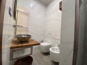 A modern bathroom with a marble backsplash, a wooden vanity, a bidet, and a large basin. - La Fontanella (Lecce)