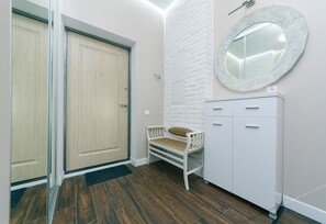 A hallway with a wooden door, a white bench, a white cabinet, and a round mirror on the wall. - VIP Apartment Company (Kyiv)