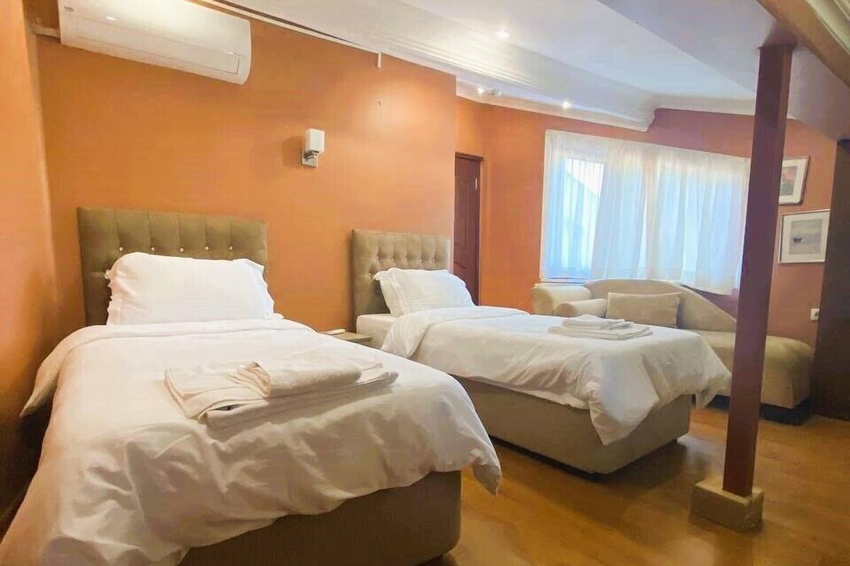 A hotel room with two beds, a window with curtains, and a wooden floor.