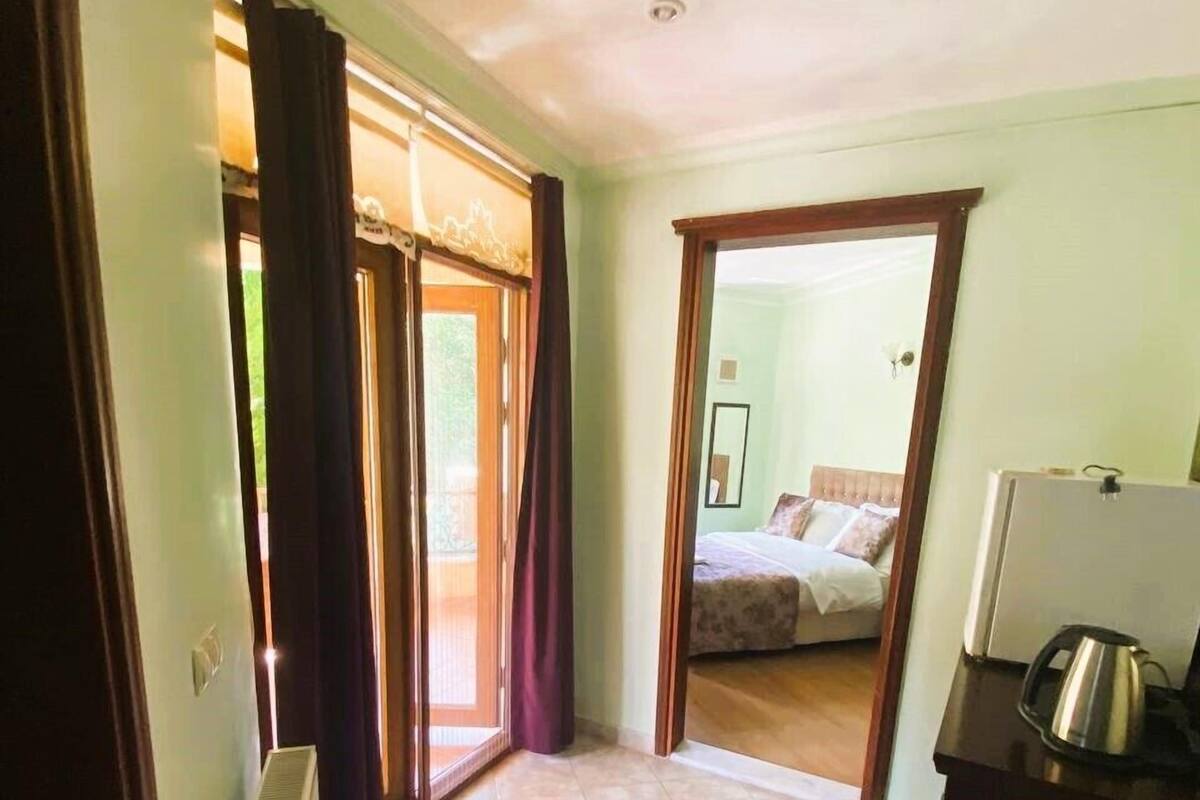 A room with a bed, a radiator, a kettle, and a door leading to another room.