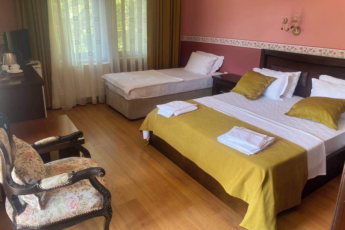 A hotel room with two beds, a wooden desk, a chair, and a window with curtains.