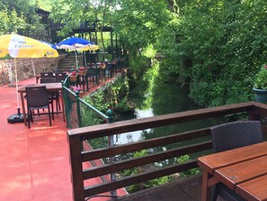 Un patio al aire libre con mesas y sillas, un canal y abundante vegetación.