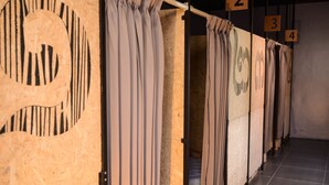 Une rangée de chambres numérotées, dotées de rideaux, de murs en bois et d’un sol carrelé.