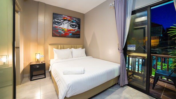 Une chambre d’hôtel avec un lit, une table de chevet, un tableau au mur et un balcon avec une chaise.