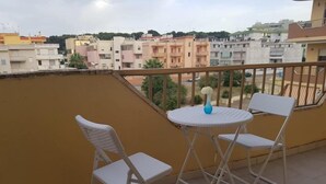 A balcony with two white folding chairs and a small round table, overlooking a residential area with various buildings. - B&B Arcobaleno (Gallipoli)