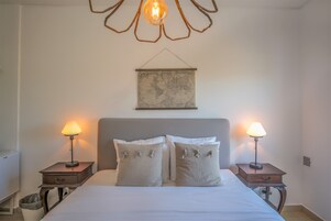 A neatly made bed with two bedside tables, each with a lamp, in a simple room with a map on the wall.