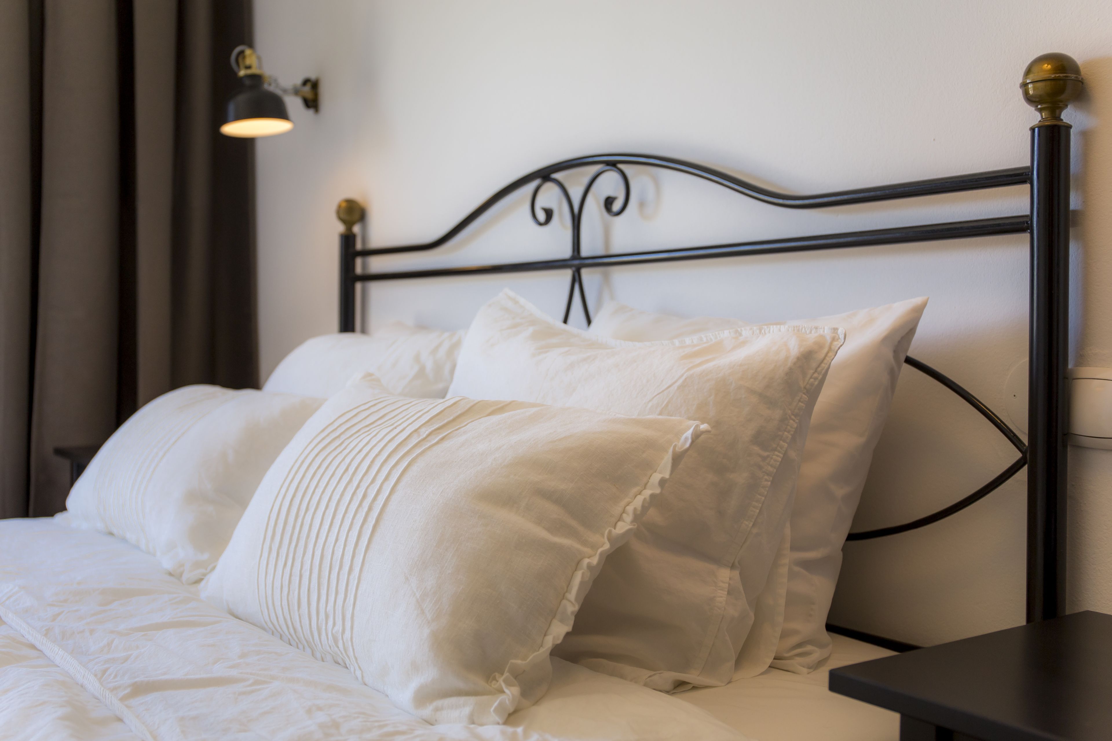 Un lit bien fait, avec du linge de lit blanc et des oreillers, une tête de lit en métal noir et une petite table de chevet.