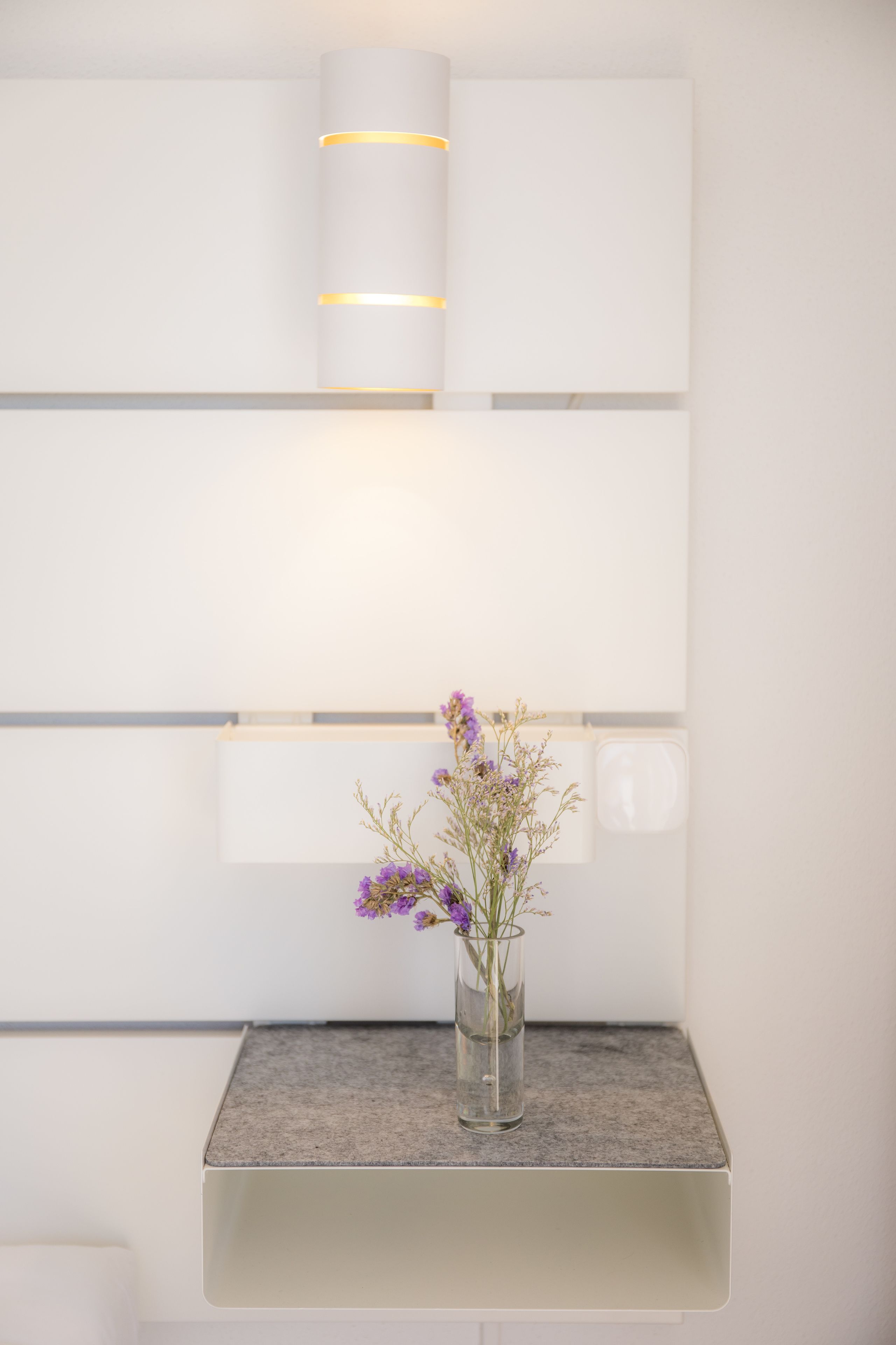 Un baño moderno con diseño minimalista, que presenta un florero de vidrio con flores moradas sobre una encimera de granito.