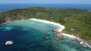 Eine Vogelperspektive einer tropischen Insel mit einem weißen Sandstrand, klarem türkisblauem Wasser und dichtem Grünland.