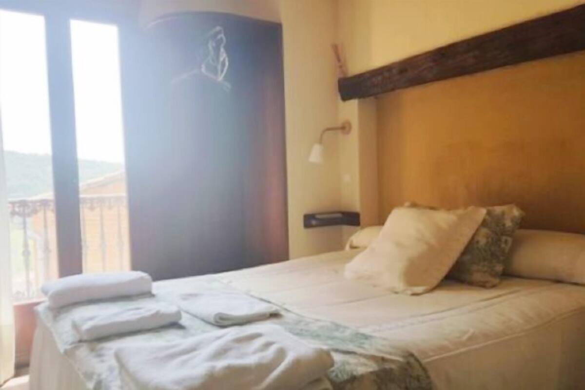 Hotellihuone, jossa on sänky, yöpöytä, ikkuna, josta on näkymä, ja ovi.