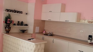 A kitchen with a white bar counter, a sink, and cabinets. There is a vase with flowers on the counter, and a shelf with decorative items. - Megas Palace Bankya (Sofia)