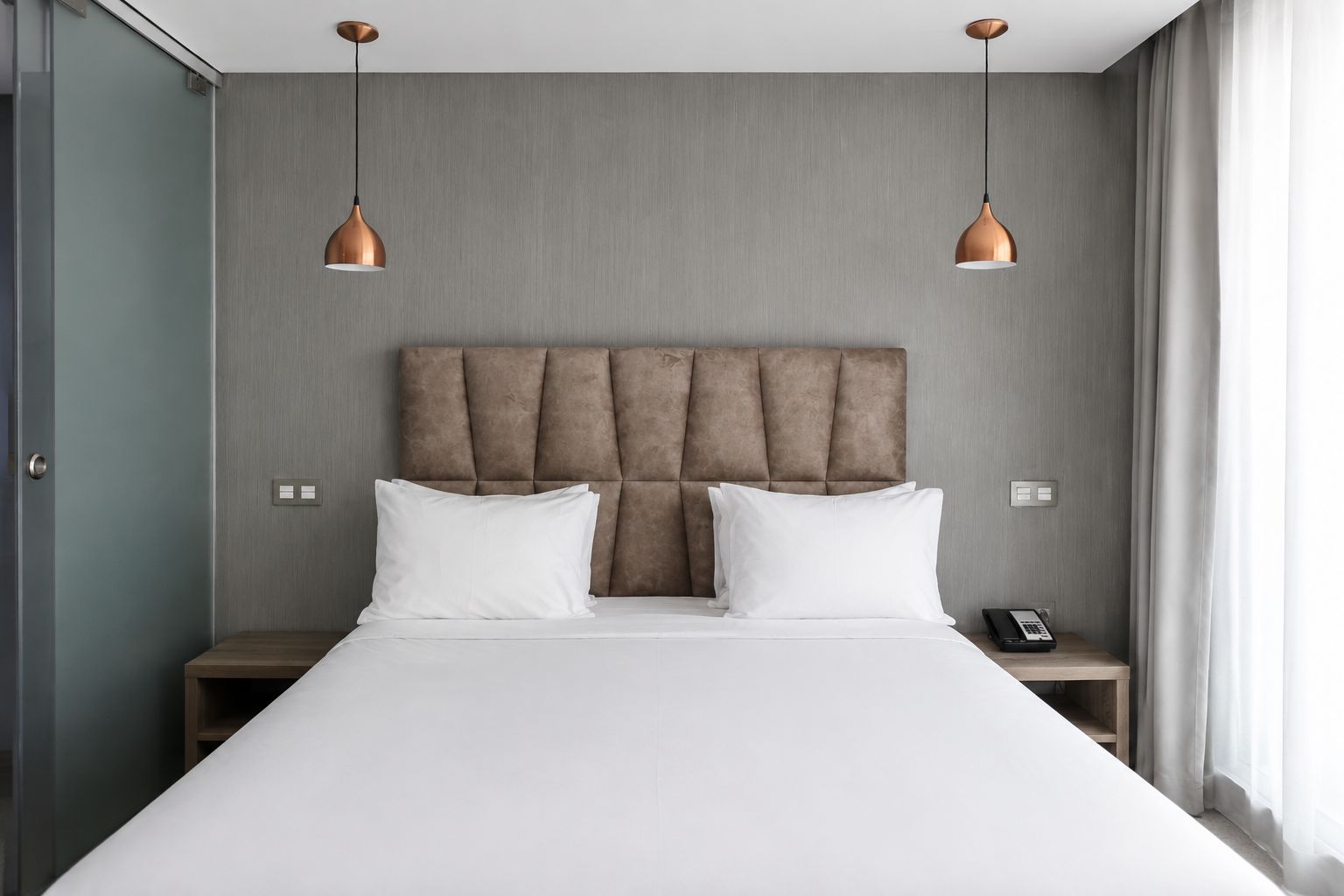 Una habitación de hotel moderna con una cama grande, dos mesitas de noche, un teléfono y dos lámparas colgantes.