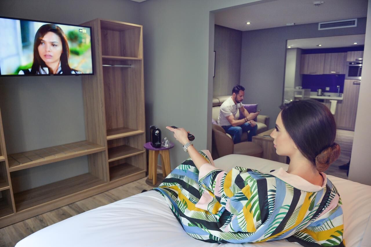 A hotel room with a bed, a television, a wooden wardrobe, and a small table with a remote control.